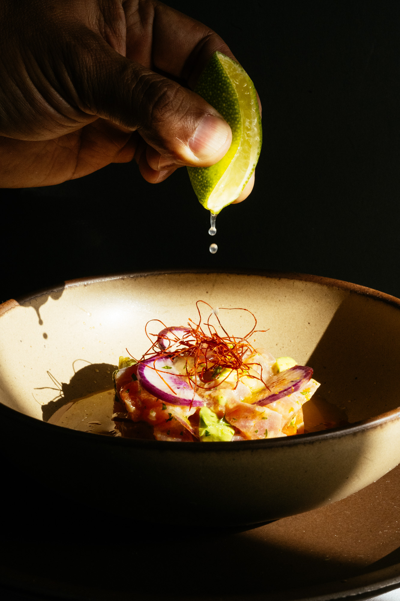 A hand squeezes fresh lime over a plated dish in a warm shaft of light at Brasa
