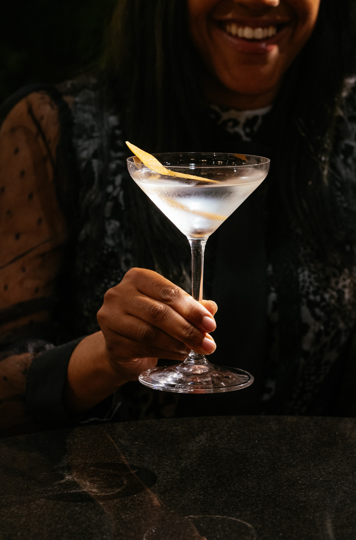 A smiling Brasa guest holding a cocktail at a dark stone table