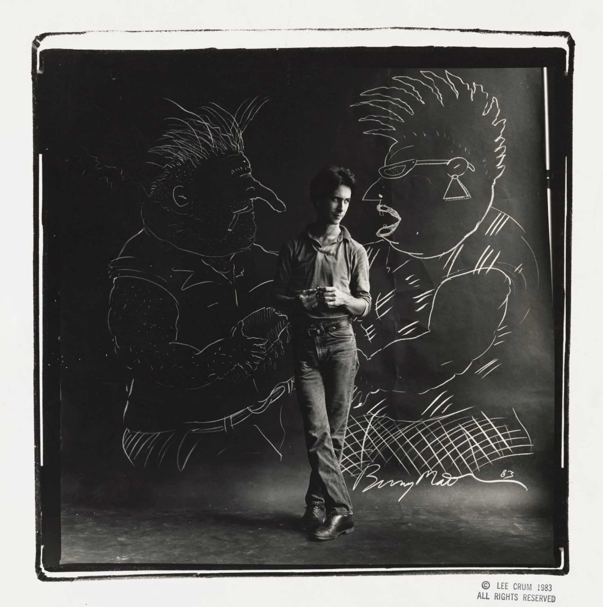 Bunny Matthews poses in front of his drawings of Vic and Nat’ly in Lee Crum’s black-and-white portrait