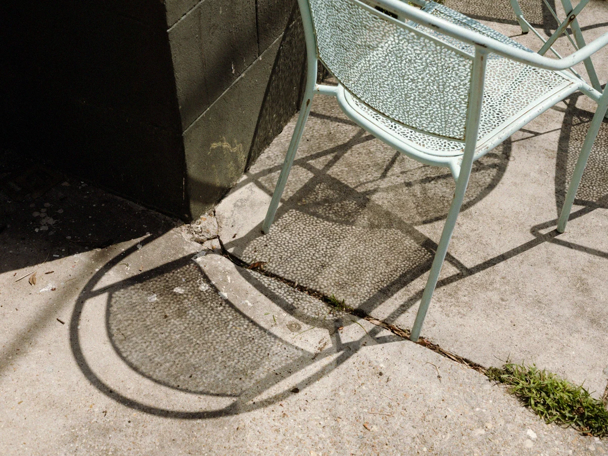 Sunlight and shadows across a café chair and sidewalk