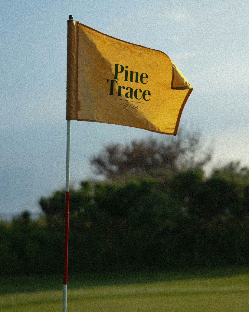 A yellow Pine Trace Golf Club flag with a dark green wordmark on the course