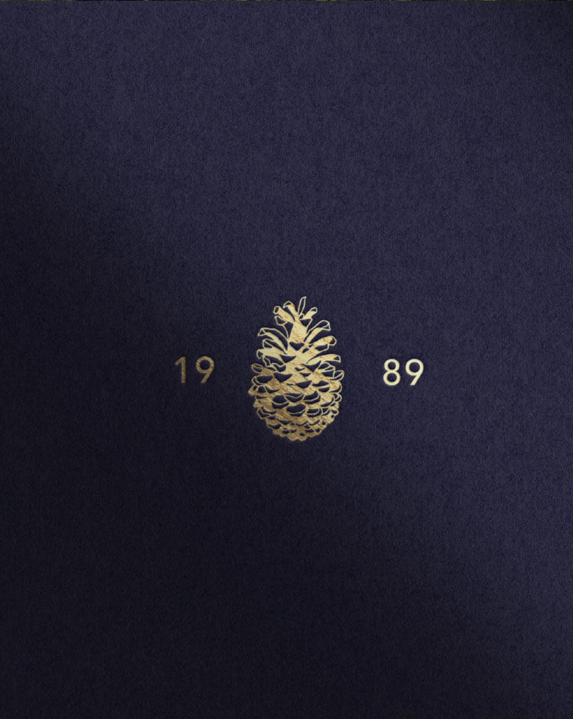 A gold Pine Trace pinecone mark and 1989 date on deep blue textured paper
