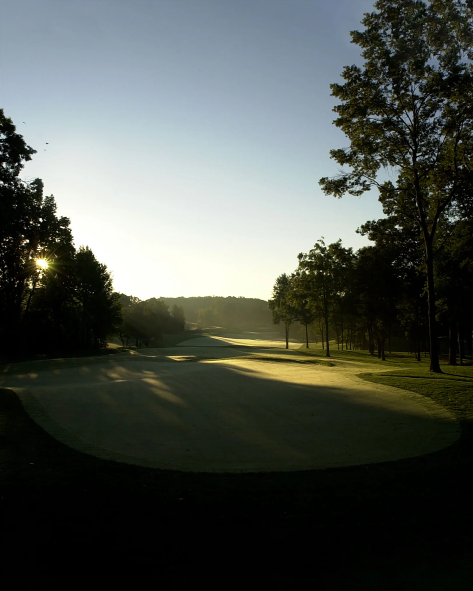 The sun rises over a green and tree-lined fairway at Shepherd’s Hollow